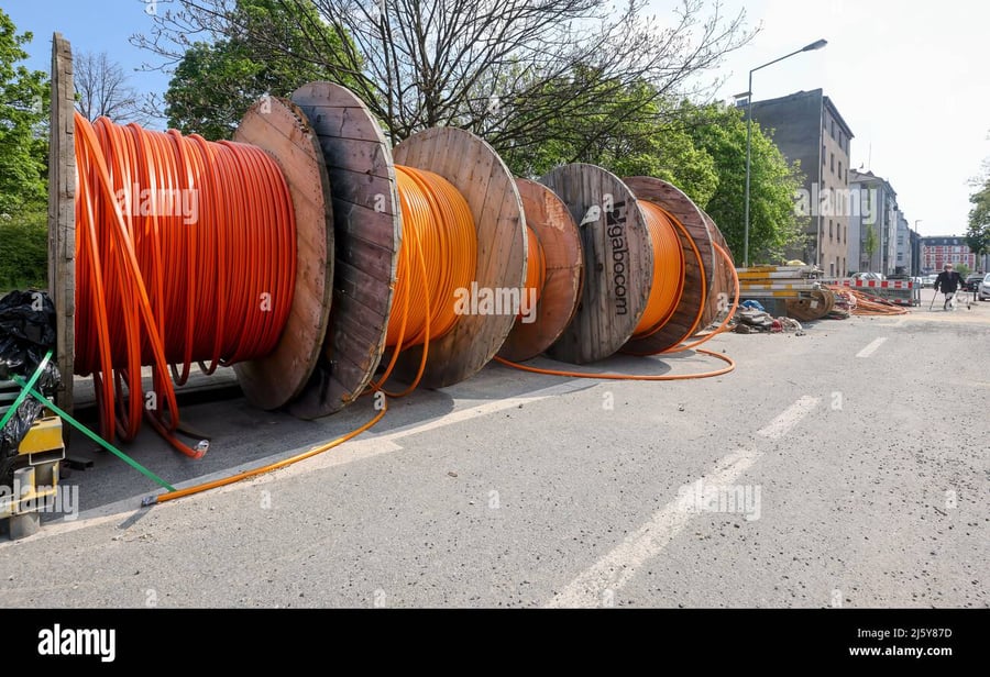 Large wooden spools of orange cable lined up on the side of a street