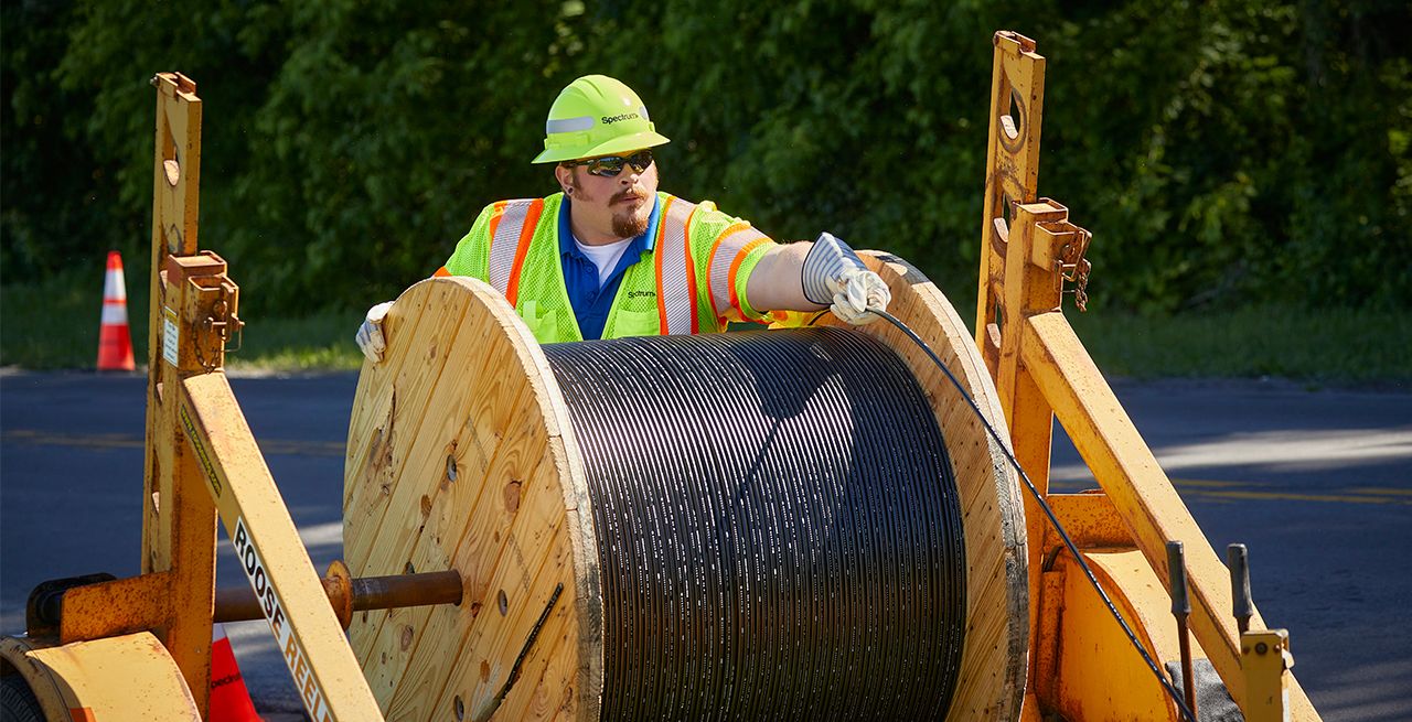 A construction worker handling a large spool of cable on a street